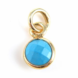 May include: A gold charm featuring a light blue gemstone. The charm has a loop for attaching to a necklace or bracelet.
