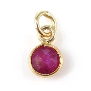 May include: A gold pendant featuring a round, faceted ruby gemstone.