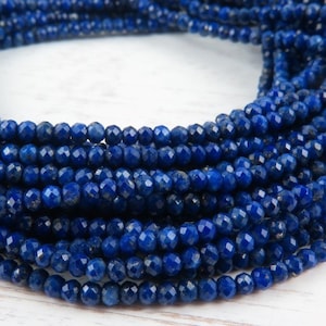 Peut inclure: Un brin de perles de lapis-lazuli bleu foncé, chaque perle est facetée et a une forme légèrement irrégulière. Les perles sont enfilées ensemble pour créer un long collier ou un bracelet.