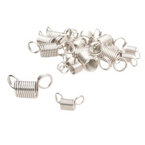 May include: A collection of silver-colored metal coil springs, each featuring a small circular loop at both ends. These cylindrical components are arranged in a loose pile, with two individual pieces placed separately in the foreground.