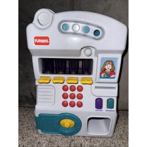 May include: A Playskool toy cash register in shades of gray, teal, yellow, and red. It features a coin slot, buttons, and a picture of a girl. The register has deposit and withdraw buttons and a coin return.