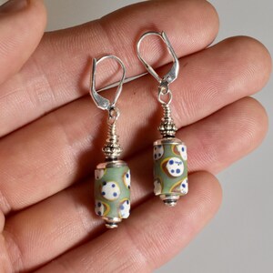 May include: A pair of dangle earrings with a light green cylindrical bead design. The beads have white and blue polka dots with yellow accents. The earrings have silver-colored lever-back closures and decorative silver-colored metal accents.