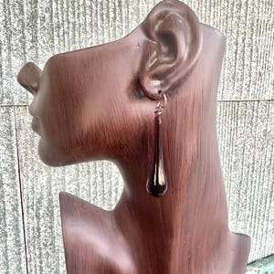 May include: A pair of dangle earrings with a teardrop-shaped purple glass pendant.