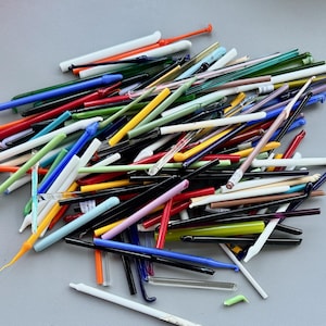 May include: A collection of colorful glass tools, including rods and tubes, in various shapes and sizes. The assortment features a wide range of colors such as red, green, blue, yellow, and black. Some tools have curved or pointed ends.