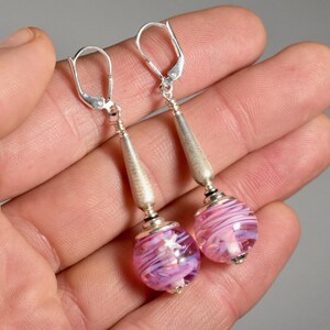 May include: A pair of silver dangle earrings with pink and white swirl glass beads. The earrings have a lever back closure.