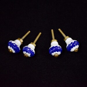 Puede incluir: Cuatro pomos de armario de cerámica blanca con diseños florales azules y tornillos dorados.