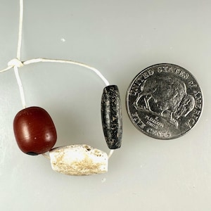 Può includere: Un filo di perline con una perla ovale rosso scuro, una perla irregolare color crema e una perla allungata grigio scuro. Una moneta da 5 centesimi americana è accanto alle perline per il confronto delle dimensioni.