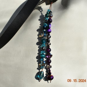 Dije de bolso brillante hecho a mano con cuentas de piedra verde azulado y violeta, cuentas de cristal bicono y rueda de vidrio, herrajes de bronce, cordón de cuero genuino