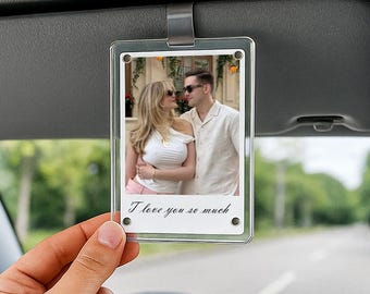May include: Clear acrylic car visor photo holder with a printed photo of a couple kissing. The photo holder has the text "I love you so much" in cursive. The holder is attached to a car visor.