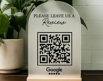 May include: A white sign with a black QR code and the text "Please leave us a review" and "Google" with five stars below the QR code. The sign is on a wooden stand.