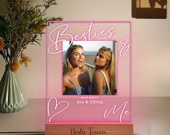 May include: A pink LED light-up photo frame with the words "Besties & Me" and "Bestie Forever". The frame holds a photo of two women and is set on a wooden base. The words "soul sister Ava & Olivia" are also visible.