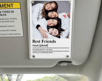 May include: A clear, rectangular photo holder with a photo of four smiling people in white coats. The text "Best Friends" is below the photo, with a definition. The holder is attached to a car visor.
