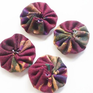 Könnte beinhalten: Vier runde Stoffknöpfe mit einem burgunderfarbenen, grünen und goldenen Blumenmuster. Die Knöpfe sind gerafft und haben einen weißen Faden in der Mitte.