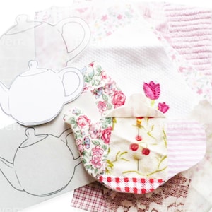 Könnte beinhalten: Eine Patchwork-Stoffteekanne mit rosa, weißen und roten Blumenmustern. Die Teekanne ist umgeben von weißem Stoff mit rosa Blumenstickerei und weißem Stoff mit rosa und weißen Streifen. Im Hintergrund befinden sich drei Papier-Teekannen.