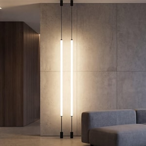 May include: Modern living room with gray sectional sofa, glass coffee table, and two vertical, illuminated light fixtures. The room features large windows with a city view and a minimalist design.