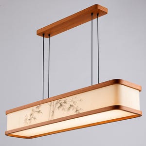 May include: Rectangular wooden pendant light fixture with a bamboo design on the shade. The light has a warm, inviting glow and is suspended from the ceiling by black cords. The fixture is made of wood and has a natural finish.