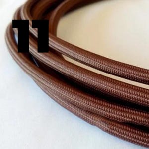 Op de afbeelding: Close-up van een bruin gevlochten elektrisch snoer, met de textuur van de stoffen bekleding zichtbaar. Het nummer "11" is zichtbaar in de afbeelding.