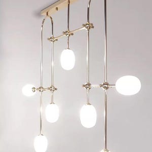 May include: A gold metal chandelier with seven white oval-shaped light bulbs. The chandelier has a modern design with a geometric pattern.