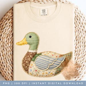May include: Cream-colored t-shirt featuring a patchwork duck design. The duck has a green checkered head, a yellow beak, and a body made of floral, striped, and patterned fabrics. The shirt has the text "COMFORT COLORS XL-TO-EG" and "KS DESIGN STUDIO".
