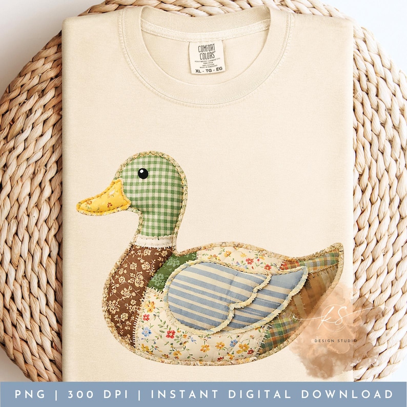 Pode incluir: Camiseta creme com um design de pato em patchwork. O pato tem uma cabe&ccedil;a xadrez verde, um bico amarelo e um corpo feito de tecidos florais, listrados e estampados. A camisa tem o texto "COMFORT COLORS XL-TO-EG" e "KS DESIGN STUDIO".