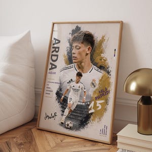 May include: A framed vertical poster featuring a portrait and action shot of soccer player Arda Güler in a white Real Madrid kit. The design includes gold and black paint splatter effects, the text ARDA GÜLER, HALA MADRID, and the number 15.