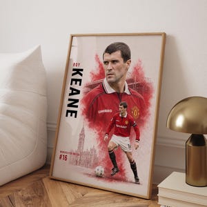 May include: A framed poster featuring a portrait and a full-body action shot of Roy Keane in a red Manchester United football kit. The design includes the text ROY KEANE, MANCHESTER UNITED, and #16, with a red watercolour effect and a clock tower.
