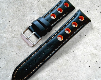 May include: Black leather watch strap with orange detailing and stitching. The strap has multiple circular perforations and a silver buckle. The watch band is designed for a classic and sporty look.