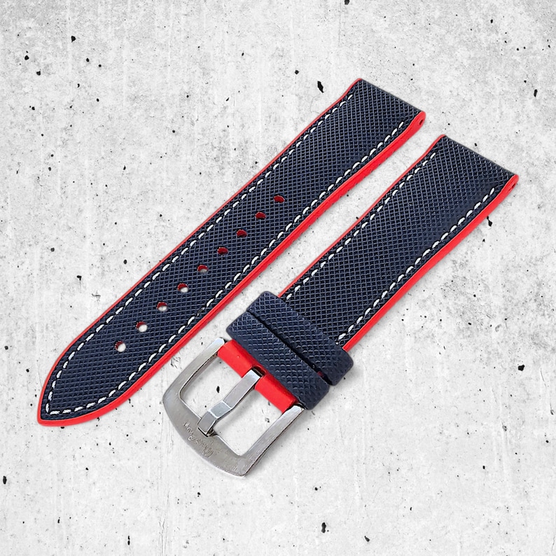 Peut inclure: Un bracelet de montre bleu avec des coutures rouges et une boucle argent&eacute;e. Le bracelet a une surface textur&eacute;e.