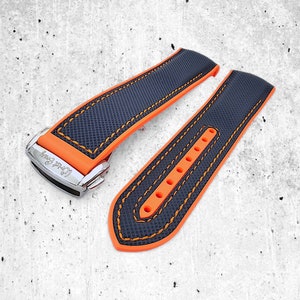 Könnte beinhalten: Ein schwarzes und orangefarbenes Uhrenarmband mit orangefarbenen Nähten und dem Text "L'Opera" auf der Schließe.