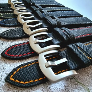 Może przedstawiać: Zbliżenie na stos czarnych pasków do zegarków z kontrastowymi kolorowymi szwami. Paski mają srebrne klamry i są wykonane z tkaniny tkanej.