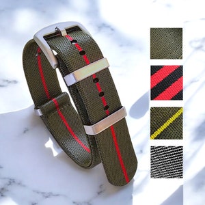 Puede incluir: Una correa de reloj de nailon verde con rayas rojas. La correa tiene una hebilla plateada y se muestra doblada por la mitad. La imagen también muestra cuatro variaciones de color diferentes de la correa.
