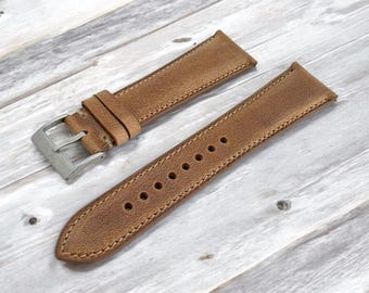 May include: Two-piece brown leather watch strap with a silver-colored buckle. The strap has visible stitching along the edges and several holes for adjustment. The leather has a distressed appearance.