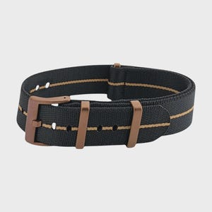 Puede incluir: Una correa de reloj negra con hebilla y presillas de bronce. La correa tiene una raya beige en el centro. La correa del reloj está hecha de un material tejido.