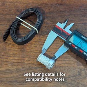 May include: A black rubber timing belt coiled and secured with a rubber band, next to a digital caliper measuring a silver pulley. The digital display shows a measurement. Text at the bottom reads "See listing details for compatibility notes."