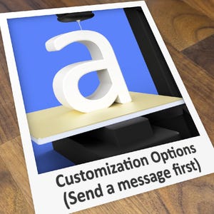 May include: A white plastic letter "a" is being 3D printed on a platform. The platform is beige and is attached to a black base. The text "Customization Options (Send a message first)" is visible at the bottom of the image.