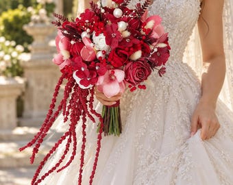 Può includere: Un bouquet di fiori con rose rosso scuro e rosa, fiori bianchi e dettagli in perla. Lunghi steli di amaranto rosso a cascata pendono dalla base, avvolta in un nastro rosso scuro. La composizione include piccole bacche ed erbe essiccate.