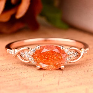 May include: A rose gold ring with a large oval-shaped sunstone and smaller clear stones set in a twisted band.