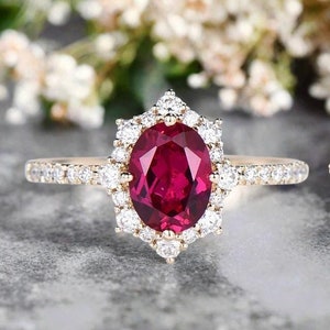 May include: A gold engagement ring featuring a large oval ruby surrounded by a halo of smaller diamonds. The band is also set with smaller diamonds.