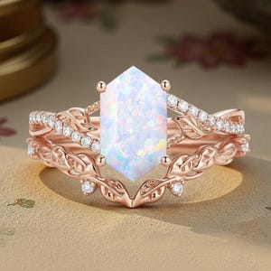May include: Rose gold ring set featuring a large, hexagonal opal center stone. The band is adorned with small, sparkling diamonds and a delicate leaf design. A matching band with diamonds completes the set, creating a beautiful engagement or wedding ring.