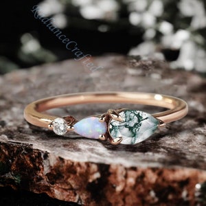 May include: A delicate gold ring with three teardrop-shaped stones. The stones are a clear diamond, a white opal, and a green moss agate.