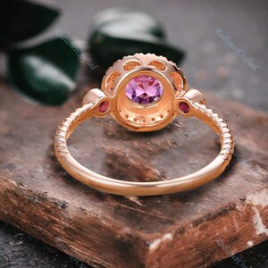May include: A rose gold ring featuring a round purple gemstone encircled by smaller clear gemstones. The ring has a delicate, twisted band.