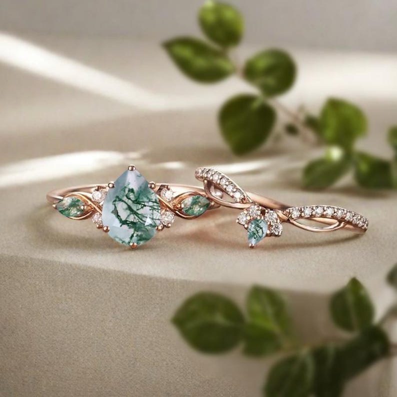 May include: Two rose gold rings. The first ring features a pear-shaped, light green gemstone with a unique pattern, surrounded by small diamonds and green gemstones. The second ring has a twisted band with small diamonds and a matching gemstone.