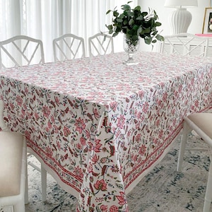 May include: White tablecloth with a pink and green floral pattern. The tablecloth is laid on a table with white chairs.