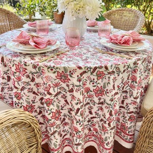 May include: A white round tablecloth with a pink and green floral pattern. The tablecloth is set with plates, glasses, and napkins.