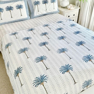 May include: White cotton quilt with a blue palm tree pattern. The quilt is on a bed with white sheets and two blue and white patterned pillowcases.