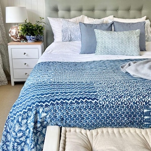 Könnte beinhalten: Eine blaue und weiße gemusterte Bettdecke mit einem weißen Bettbezug und Kissen mit blauen und weißen Mustern. Das Bett steht an einer weißen Wand mit einem weißen Nachttisch und einer Lampe.