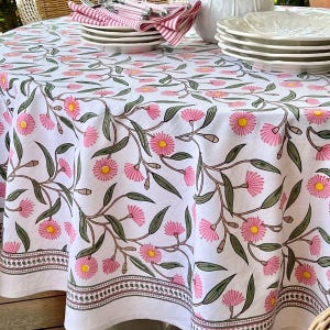 May include: White tablecloth with a repeating pattern of pink flowers, yellow centers, and green leaves. The tablecloth has a decorative border and is set with plates, napkins, and silverware.