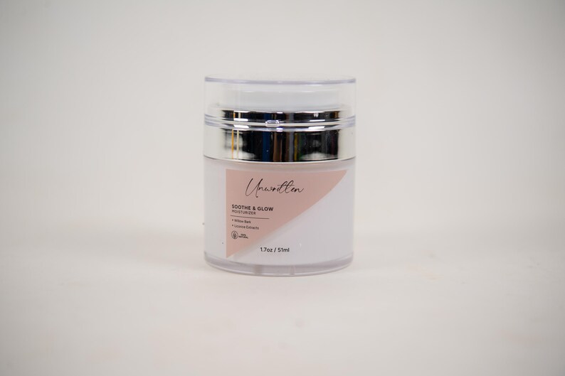 Puede incluir: Un tarro de pl&aacute;stico blanco y rosa con tapa plateada. El tarro contiene una crema hidratante etiquetada como "Unwritten Soothe & Glow Moisturizer 1.7 oz / 50 ml".