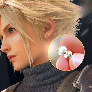 May include: A close-up of a silver stud earring with a pearl-like center. The earring is shown in the ear of a person with blonde hair and a gray turtleneck. A second earring is visible in the ear.