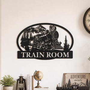 Peut inclure: Décoration murale en métal noir représentant une locomotive détaillée dans un cadre ovale, sur fond de montagnes et de forêt. Les mots "TRAIN ROOM" sont affichés en dessous. Une pièce décorative pour les passionnés de trains.